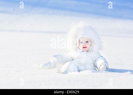 Süße kleine Baby in eine weiße Jacke im Schnee spielen Stockfoto