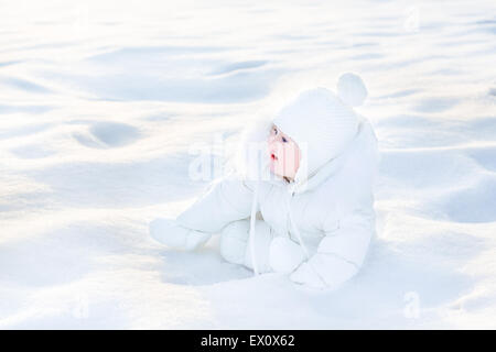 Süße kleine Baby in eine weiße Jacke im Schnee spielen Stockfoto