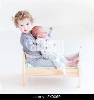 Lustige Kleinkind Mädchen spielen mit ihrem Neugeborenen Baby Bruder in ein Spielzeug-Bett Stockfoto