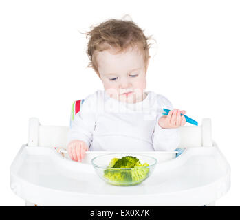 Süße lustige Kleinkind in einem weißen Hochstuhl Essen ihr Gemüse für das Mittagessen, isoliert auf weiss Stockfoto