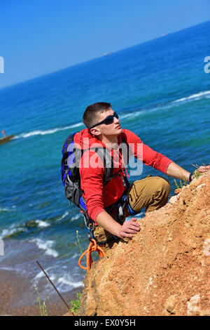 Mann klettert auf einer Klippe über blaue Meer Hintergrund Stockfoto