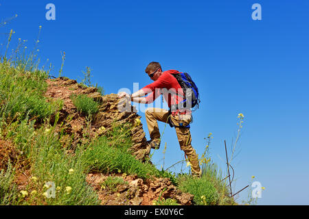 Mann klettert auf einer Klippe über blauen Himmelshintergrund Stockfoto