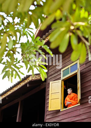 Ein junger Mönch blickt aus dem Fenster seines Zimmers in Vientiane, Laos, Wat Si Muang, Kanaren Stockfoto