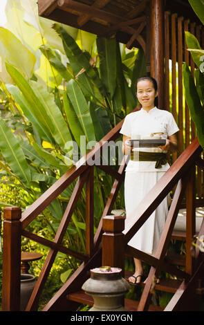 Ein Spa-Therapeuten trägt Tee hinunter die Schritte von einem der vier Behandlungsräume im La Residence Phou Vao. Luang Prabang, Laos. Stockfoto