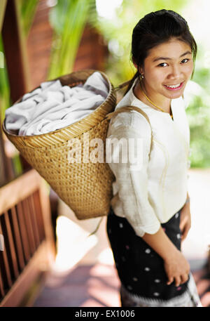 Ein Zimmermädchen trägt Handtücher in einem Korb auf dem Rücken bei 3 Nagas Alila Hotels. Luang Prabang, Laos. Stockfoto