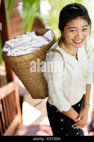 Ein Zimmermädchen trägt Handtücher in einem Korb auf dem Rücken bei 3 Nagas Alila Hotels. Luang Prabang, Laos. Stockfoto