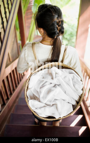 Ein Zimmermädchen trägt Handtücher in einem Korb auf dem Rücken bei 3 Nagas Alila Hotels. Luang Prabang, Laos. Stockfoto