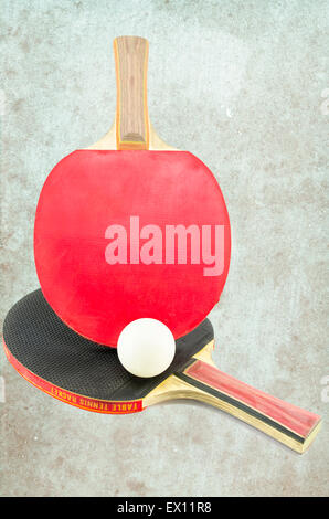 Zwei Ping-Pong-Schläger und einen Ball auf einen konkreten Hintergrund Stockfoto