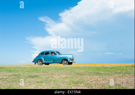 VARADERO, Kuba - 7. Juni 2011: Klassische amerikanische Oldtimer Laufwerke flach Küstenstraße gegen eine tropische Wolken. Stockfoto