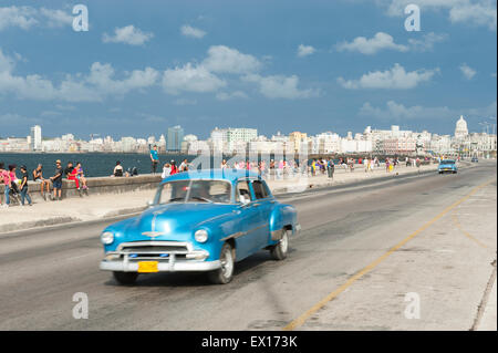 Havanna, Kuba - 18. Mai 2011: Klassisch blau American Taxi fährt neben Massen der Kubaner entspannend auf dem Malecon. Stockfoto