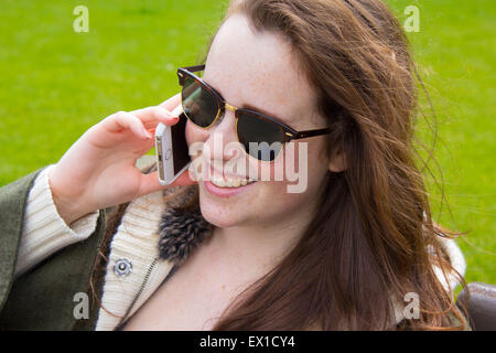 Schöne, junge Mädchen lächelnd und sprechen auf dem Handy, sitzen auf der Bank außerhalb, Nahaufnahme portrait Stockfoto