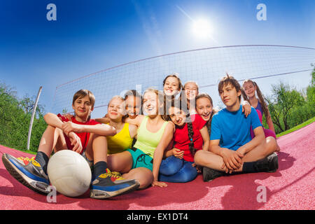 Glückliche Jugendliche, die auf Spiel-Volleyball-Platz sitzen Stockfoto