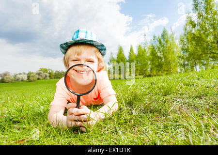 Glücklich lächelnd durch Lupe Junge legt auf Rasen Stockfoto