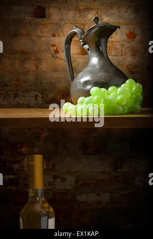 Stillleben mit einem Metall Krug und Weintraube auf einem Regal vor einem abgenutzten Ziegel Wand Hintergrund.  Es gibt auch eine Flasche Wein Stockfoto