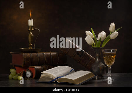 Stillleben mit eine aufgeschlagene Bibel, umgeben von Büchern, eine Kerze, Tulpen in einer Vase, ein Glas Wein, Trauben und eine Tasche zu sehen. Stockfoto