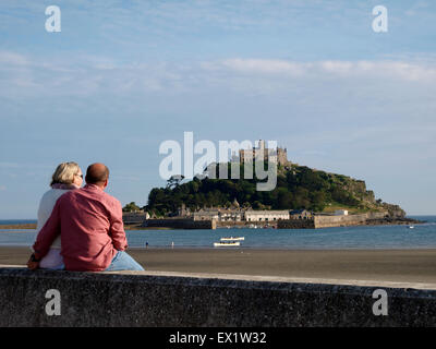 Applying paar saß auf dem Deich mit Blick auf St. Michaels Mount, Marazion, Cornwall, UK Stockfoto