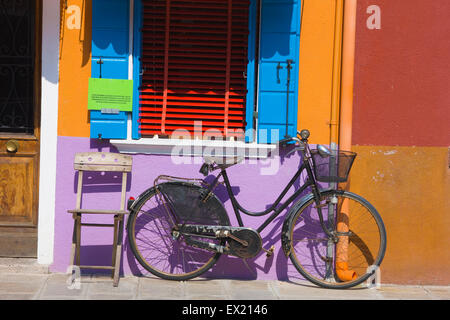 Altes Fahrrad und Stuhl gelehnt eine bunt bemalte Wand, Insel Burano, Venedig, Italien Stockfoto