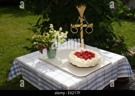 Hausgemachter Erdbeerkuchen auf Tisch mit Blumen geschmückt und ein Mittsommer-Pole in einem Garten Stockfoto