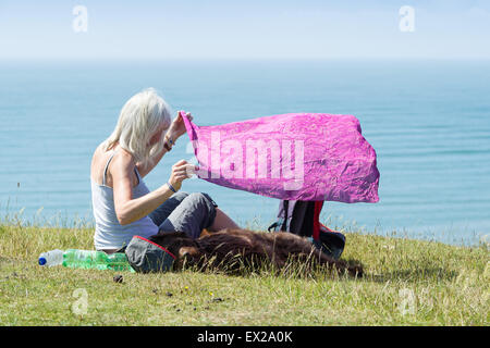 Eine Frau schützt ihren Hund vor der Sonne auf einer Klippe mit Blick auf Rhossili Bay Strand, Gower Peninsula, South Wales, Australia Stockfoto