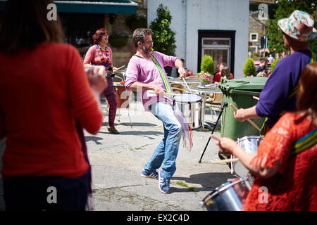 Ein Mann spielt Schlagzeug in einer Samba-Band, umgeben von anderen Spielern auf einer Straße in Skipton tagsüber Schafe. Stockfoto