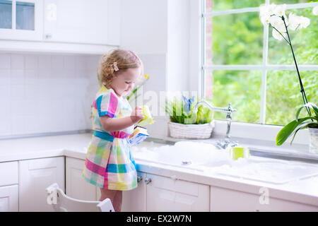 Kind abwaschen. Kinder waschen Teller und Tassen. Kleines Mädchen mithilfe in der Küche spielen mit Wasser und Schaum in eine weiße Wanne Stockfoto