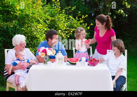 Große Familie mit Kindern haben Mittagessen im Freien. Eltern mit 3 Kindern und Großmutter Speisen im Garten. Picknick für Mutter, Vater, Stockfoto