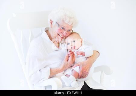 Schöne Großmutter singt ihrem Neugeborenen Enkel sitzen in einem weißen Schaukelstuhl Stockfoto