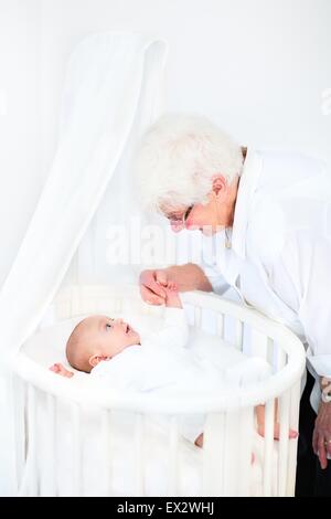 Glücklich liebende Großmutter im Gespräch mit ihrem Neugeborenen Enkel in einer weißen runden Krippe Stockfoto