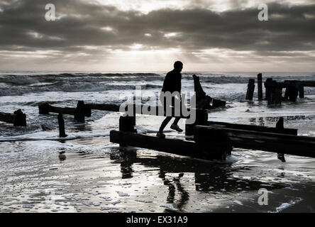 Jogger, springen über alten Holzsteg am Strand bei Sonnenaufgang. Die Landzunge, Hartlepool, England, UK Stockfoto