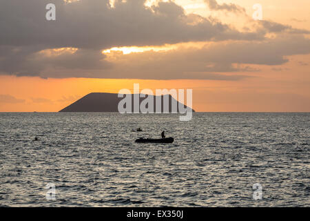 Ein Fährmann ist gegen die untergehende Sonne und einen kleinen Vulkan aus North Seymour auf den Galapagos Inseln Silhouette. Stockfoto