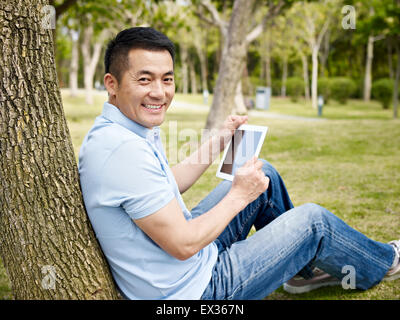 asiatischer Mann in Freizeitkleidung mit Tablet-PC im Freien im Park. Stockfoto