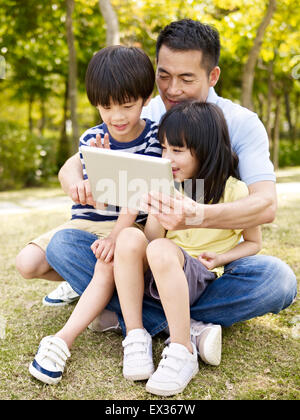 Vater und Kinder mit dem Ipad im park Stockfoto