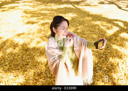 Senior japanische Frau, die ein Selbstporträt in einem Stadtpark im Herbst Stockfoto