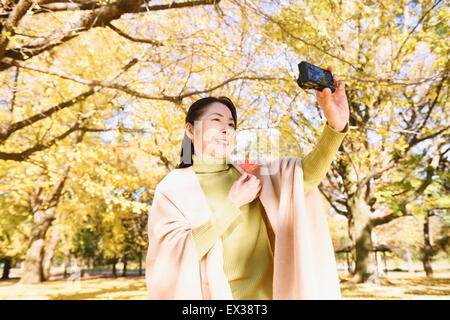 Senior japanische Frau, die ein Selbstporträt in einem Stadtpark im Herbst Stockfoto