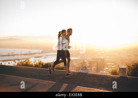 Aufnahme des jungen Paares auf Hügel Strecke außerhalb der Stadt.  Junger Mann und Frau Joggen morgens mit hellem Sonnenlicht. Stockfoto