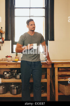 Portrait Mann steht in der Küche hält eine Tasse Kaffee wegsehen in Gedanken. Entspannten Jüngling Kaffeetrinken zu Hause in Stockfoto