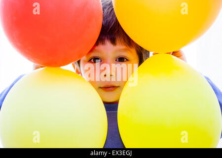 Kaukasier Kind, Junge, 6-7 Jahre alt, vier Ballons Rahmen um seinen Kopf mit seinem Gesicht spähen durch die Mitte zu bilden, Auge - Kontakt. Stockfoto