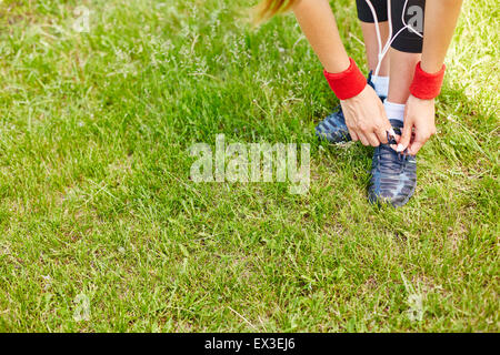 Sportliche Mädchen binden Schnürsenkel von ihren Sneakers im stehen auf dem Rasen Stockfoto