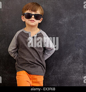 Porträt von intelligenten kleinen Jungen mit Sonnenbrille schmunzelnd. Cooler Kerl in den Farbtönen stützte sich auf einer Tafel, Blick in die Kamera Lächeln w Stockfoto