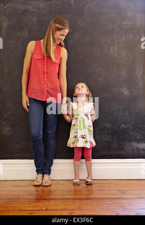 Voller Länge Schuss süße kleine Mädchen mit ihrer Mutter zu Hause stehen. Mutter und Tochter sahen einander an einer Wand Stockfoto