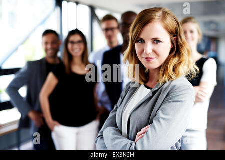 Junge weiße Frau Executive mit verschränkten Armen stand vor der Kollegen an der Kamera grinsend Stockfoto