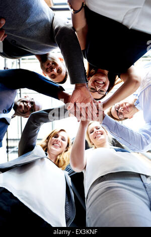 Mitarbeiterinnen und Mitarbeiter stehen in einem Kreis Hände zusammen in die Kamera schaut Stockfoto