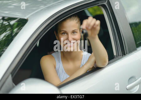 Junge hübsche Frau sitzt in ihrem Auto, lächelnd in die Kamera während zeigen, Schlüssel in die Hand. Stockfoto