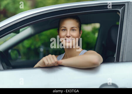 Hübsche junge Frau sitzt im Auto, während stützte sich auf das offene Fenster in die Kamera Lächeln Stockfoto