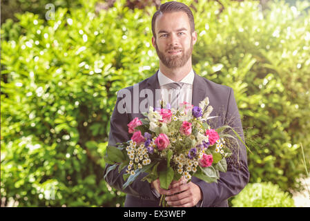 Hübscher bärtiger junger Mann in einem Anzug mit einem Bouquet von frischen Blumen, möglicherweise einen Verehrer oder Beau ruft bei einem Date, Valentine Stockfoto