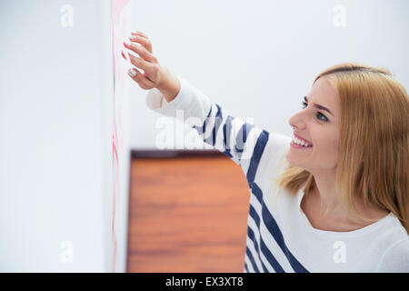 Glückliche junge Frau liest Aufkleber auf graue Wand im Büro Stockfoto