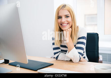 Fröhliche junge weibliche Designer am Tisch sitzen im Büro und Blick in die Kamera Stockfoto