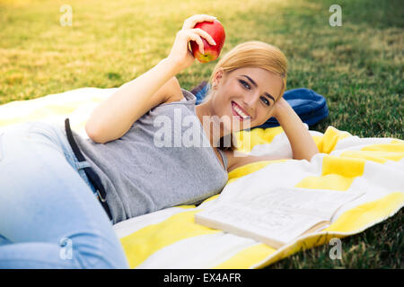 Junges Mädchen liegend mit Apfel in Park und Blick in die Kamera Lächeln Stockfoto