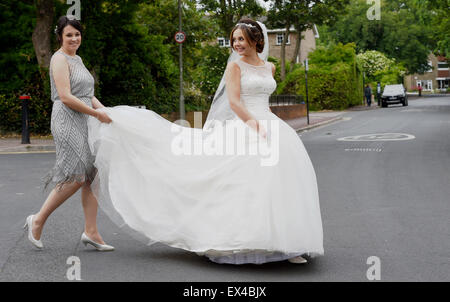 Schöne junge Frau Braut im weißen Kleid an ihrem Hochzeitstag von ihre Brautjungfer Straßenseite geholfen Stockfoto