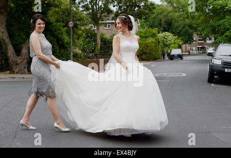 Schöne junge Frau in weißem Kleid Braut an Ihrem Hochzeitstag auf der anderen Straßenseite half durch ihre Brautjungfer sein Stockfoto